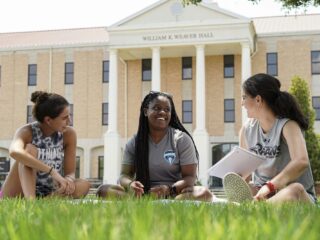 a group of women sitting on grass in front of a building