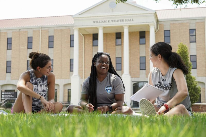 a group of women sitting on grass in front of a building