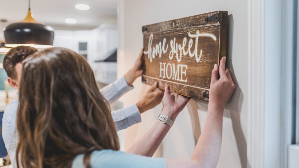 Couple hanging wooden “home sweet home” sign on a wall