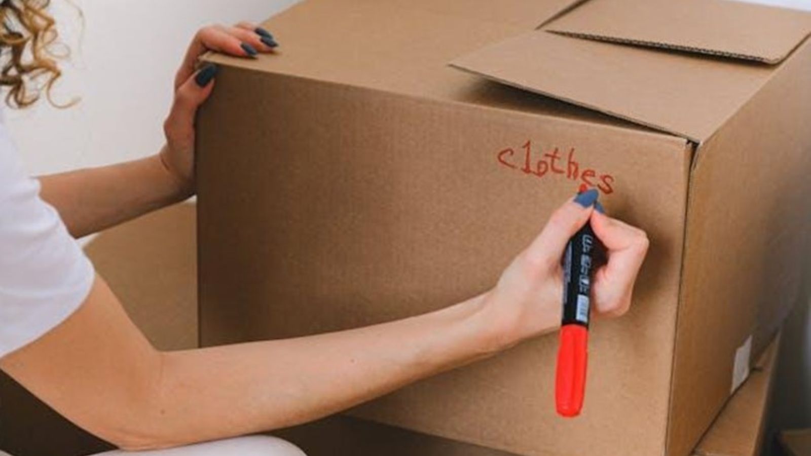 A woman writing on a cardboard box with a red marker