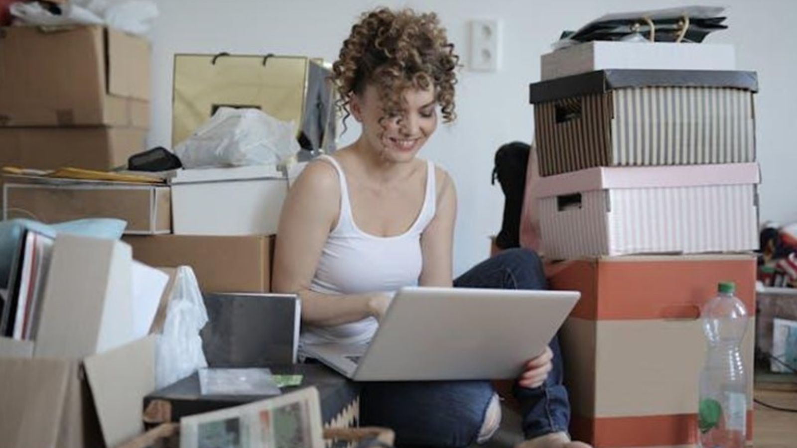 A woman holding a laptop while sitting on the floor among boxes