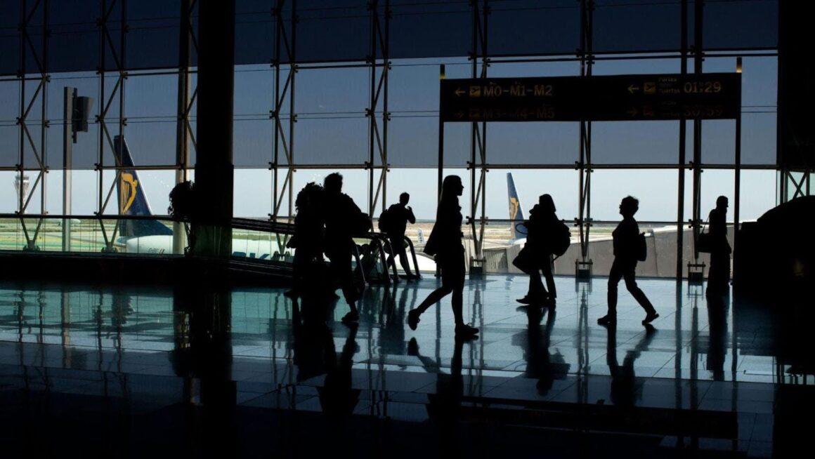 Silhouetted travelers walking through airport terminal.
