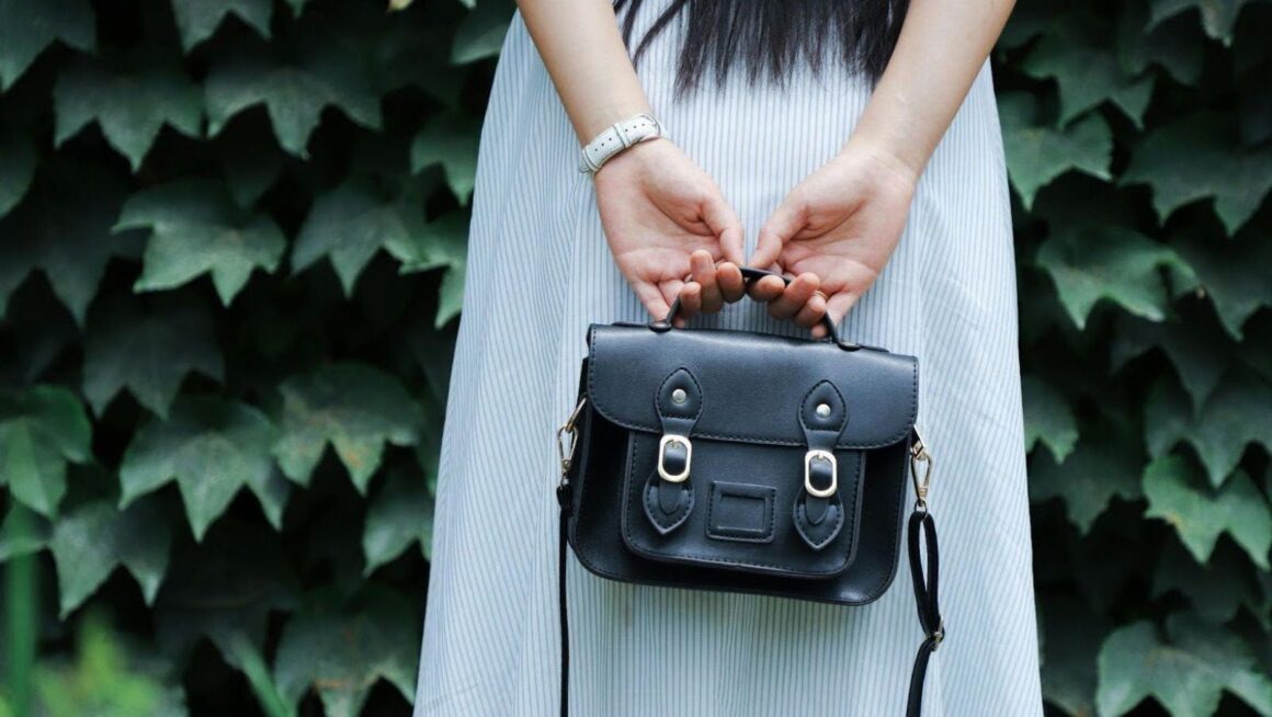 Hands holding black satchel behind dress.