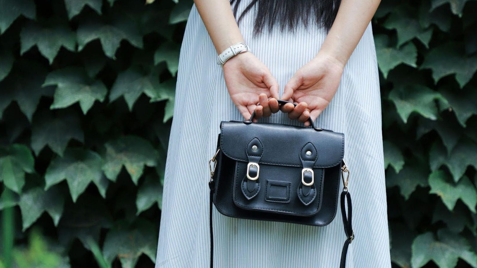 Hands holding black satchel behind dress.