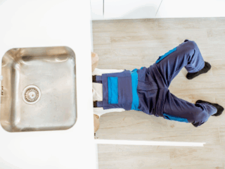 Plumber fixing a kitchen sink drain at home, showing a local plumbing expert repairing under-sink pipes for new homeowners.